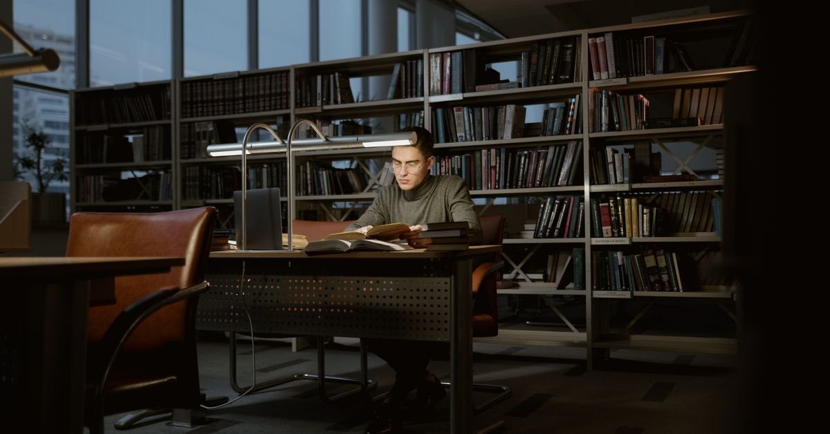 Estudante lê livros em mesa de biblioteca