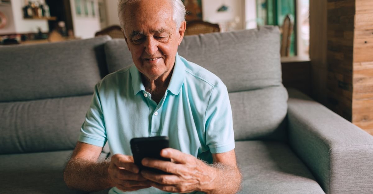 Homem idoso sentado no sofa consultando o celular