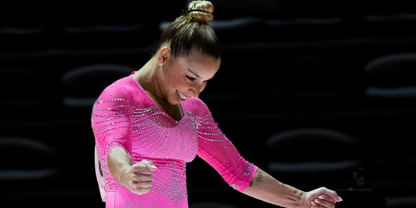 A ginasta Flávia Saraiva, de collant rosa, sorri durante apresentação em competição de ginástica artística