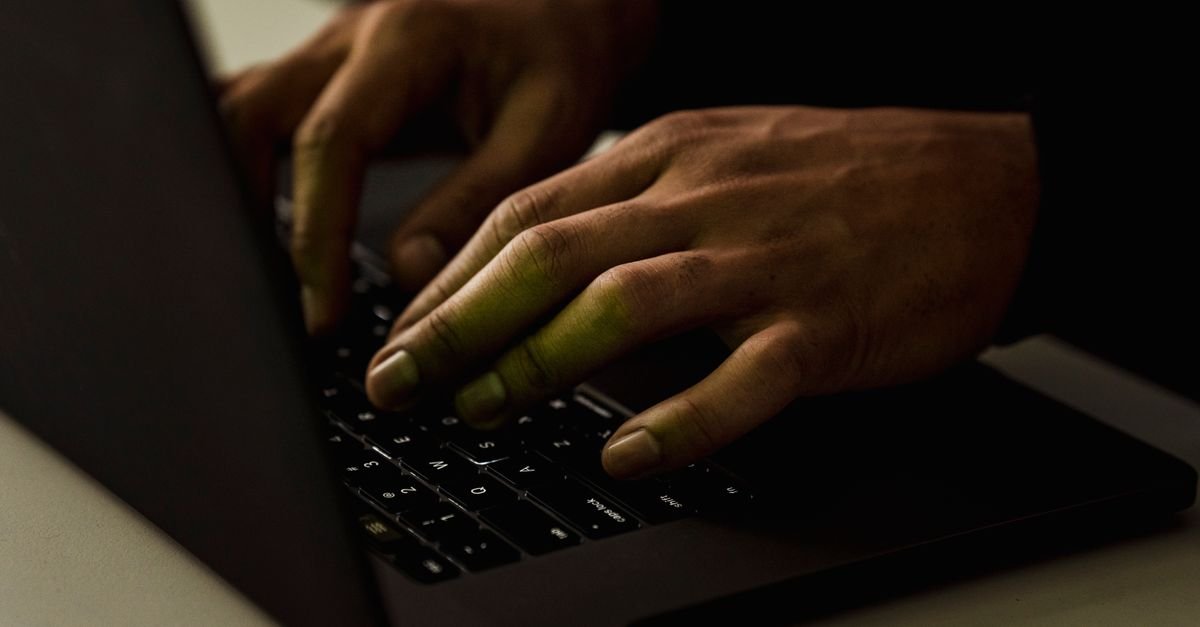 Mãos digitando no teclado de um notebook em ambiente escuro, em imagem que ilustra fraude digital