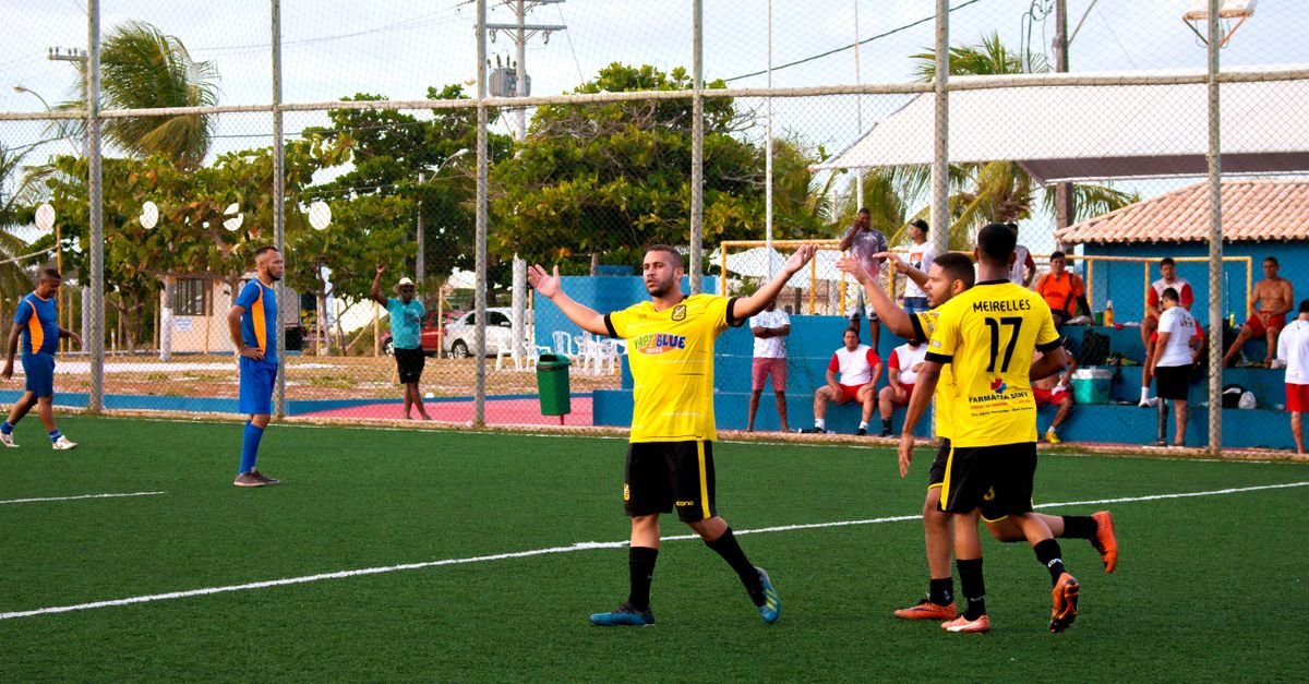 Jogadores de time amador de futebol comemoram gol em campo comunitário