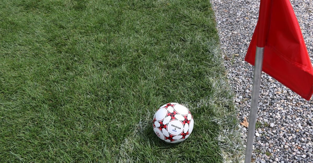 Bola de futebol parada no gramado ao lado da bandeira de escanteio