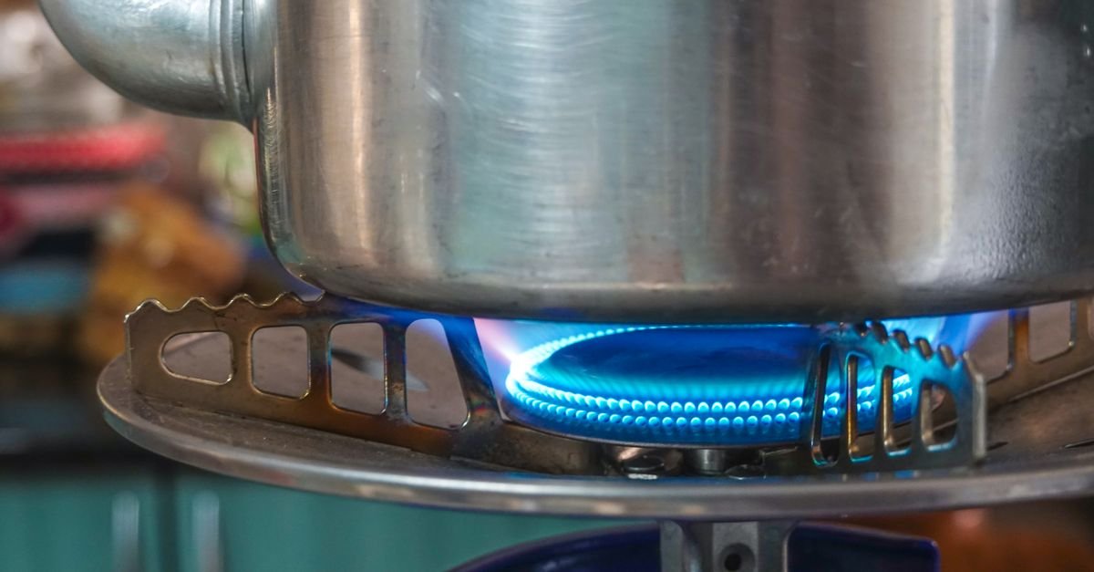 Panela de alumínio sobre a chama azul de um fogão a gás, em closeup