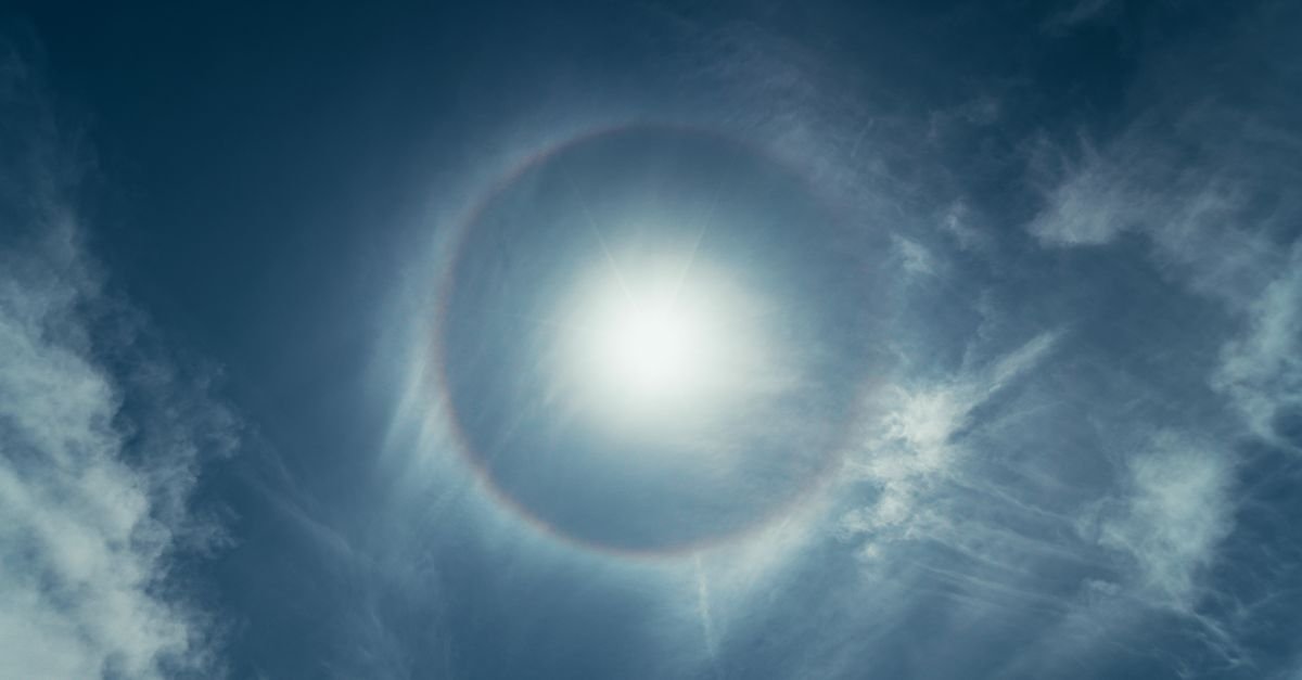 Anel luminoso de halo solar em volta do Sol em céu azul com nuvens finas