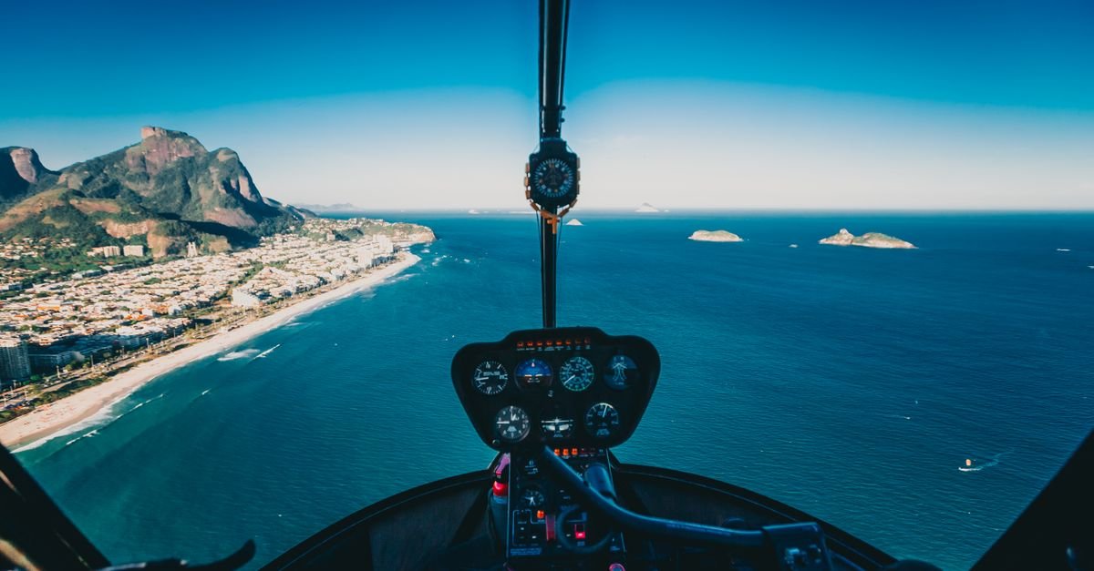 Vista da cabine de um helicóptero em voo sobre a orla e o mar do Rio de Janeiro