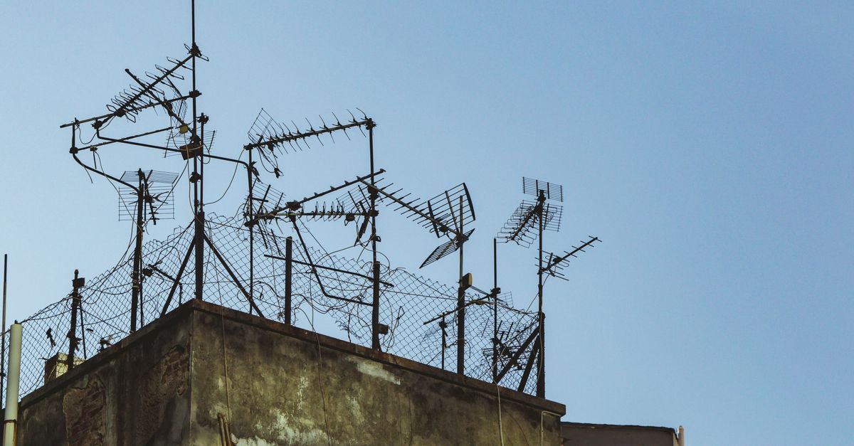 Antenas de televisão instaladas no topo de um prédio contra o céu azul