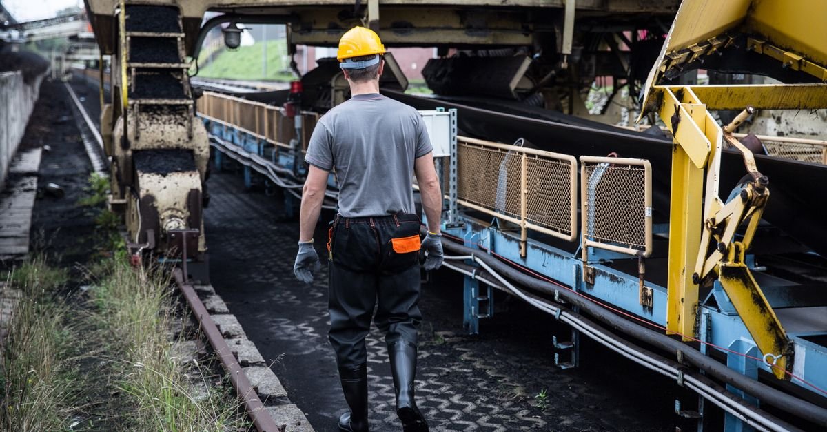 Trabalhador com capacete de segurança caminha entre esteiras e máquinas em área industrial