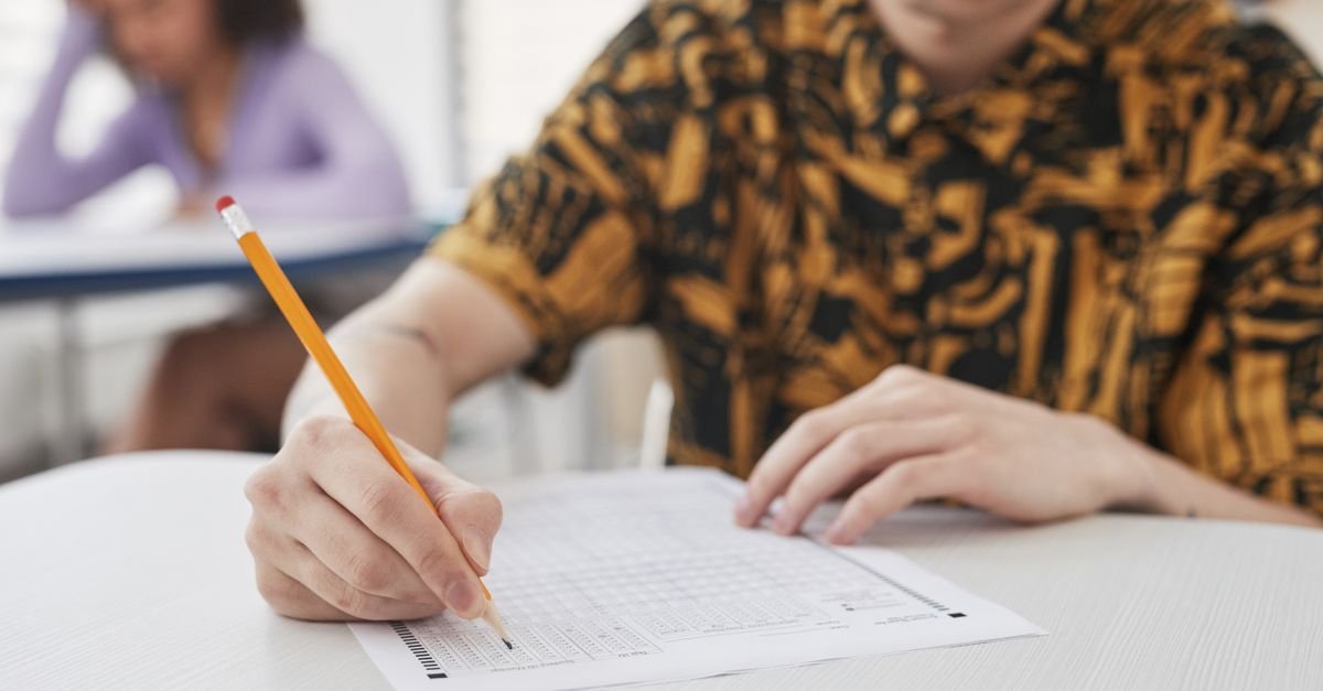 Estudante preenche cartão-resposta de prova com lápis sobre carteira escolar