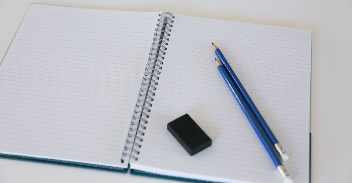 Caderno espiral aberto sobre mesa, com dois lápis azuis e uma borracha