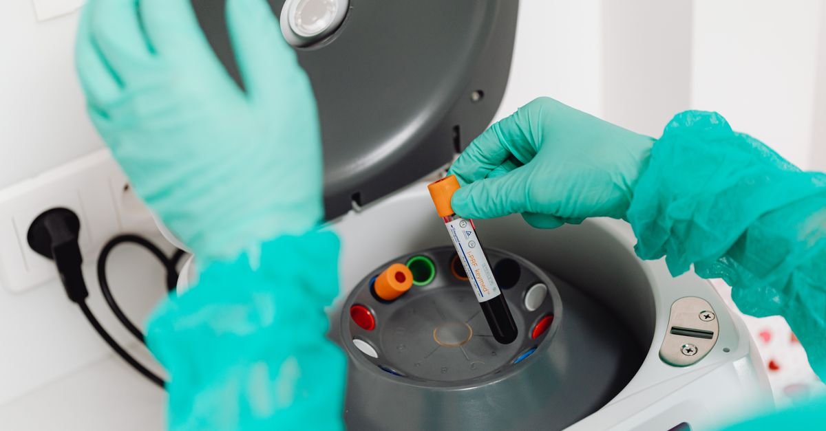 Técnico de laboratório com luvas coloca tubo de amostra em centrífuga