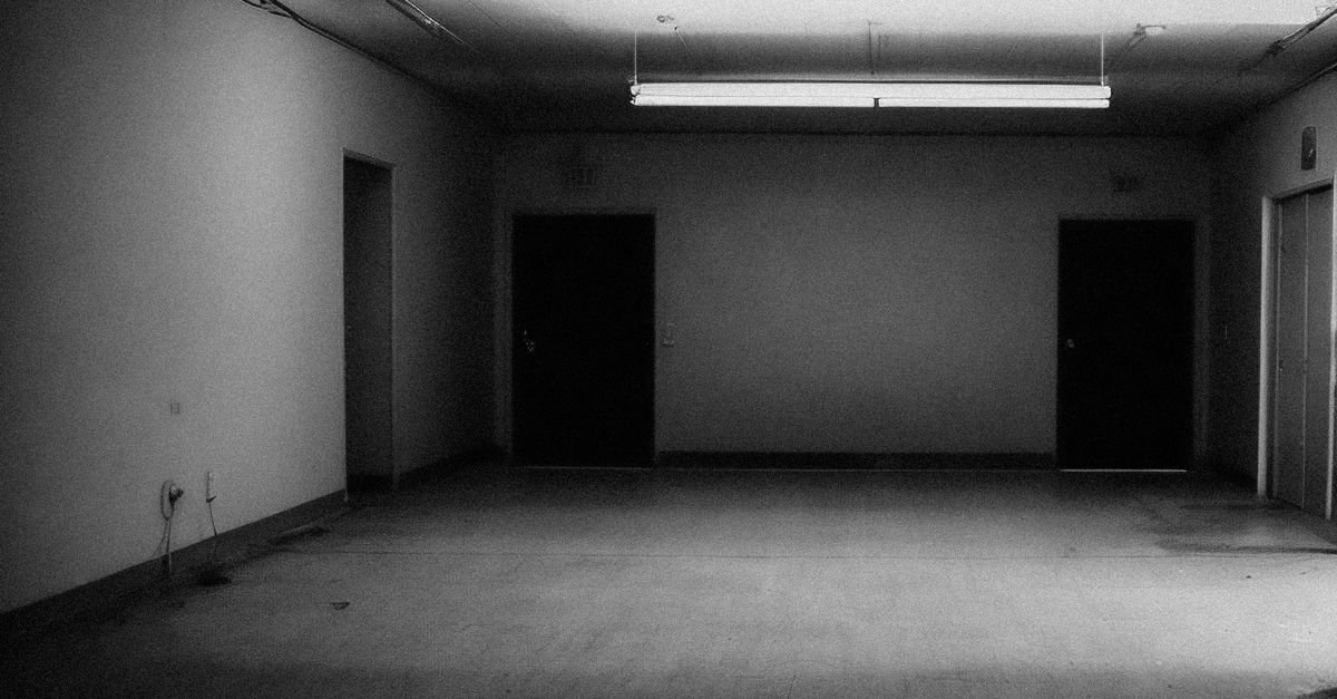 Sala comercial vazia e mal iluminada, com portas fechadas e piso de concreto