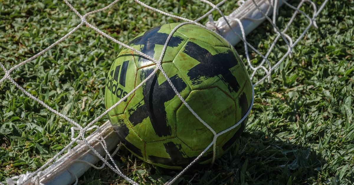 Bola de futebol na rede do gol em campo de grama