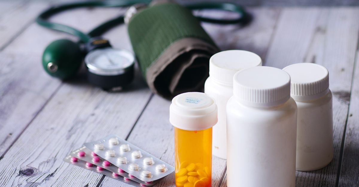 Frascos de medicamento, cartela de comprimidos e aparelho de pressão sobre mesa de madeira