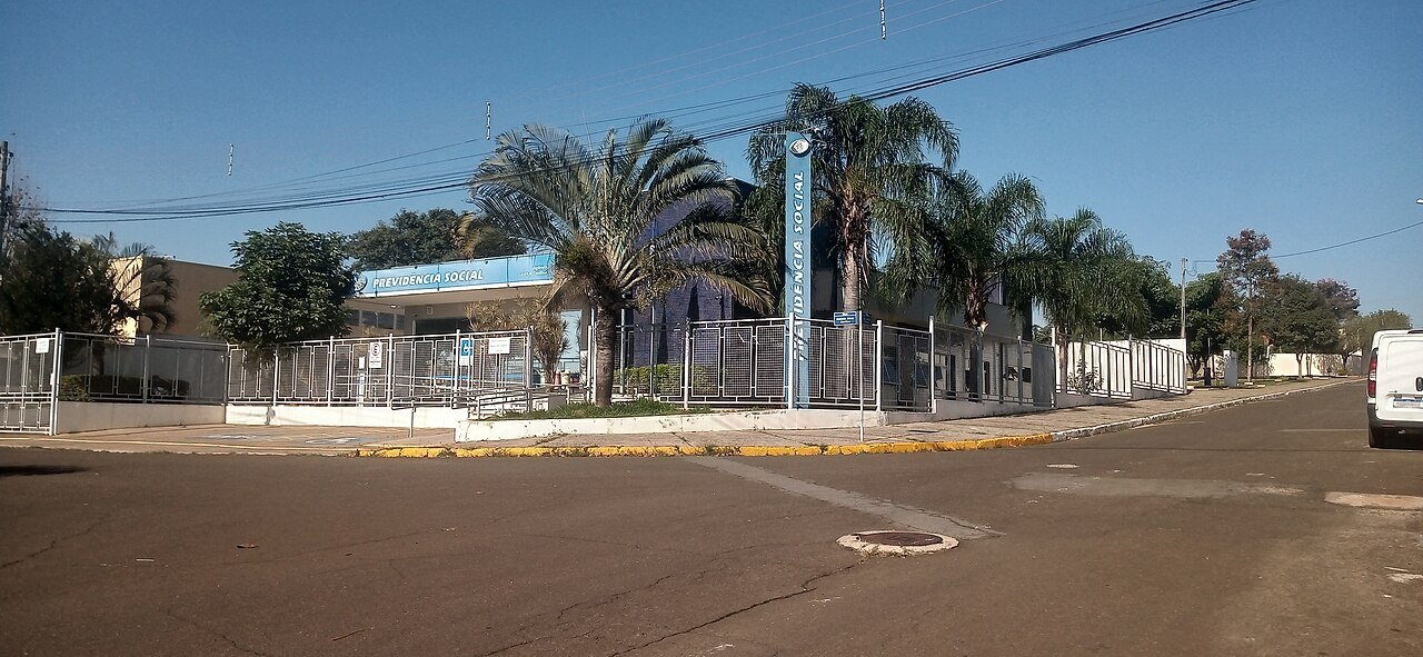 Fachada de uma agência da Previdência Social, com placa azul e grades na entrada
