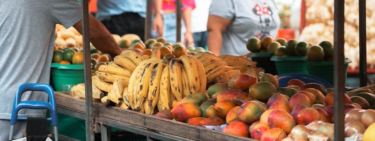 Barraca de feira com bananas e mangas expostas em caixotes de madeira