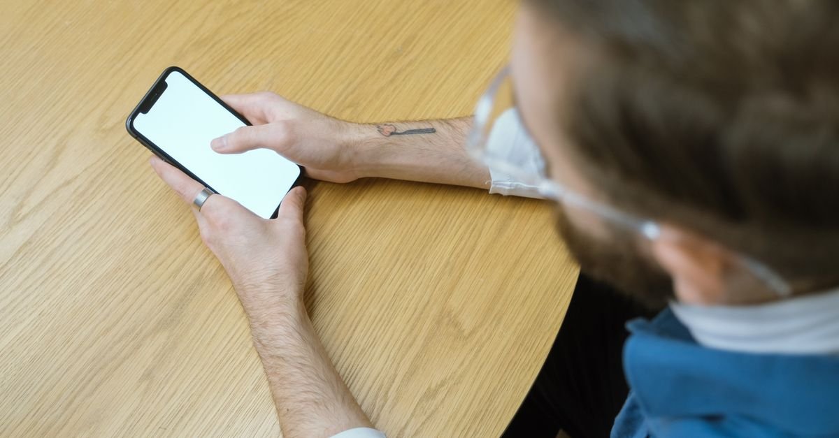 Pessoa sentada a uma mesa de madeira segura um celular com a tela em branco