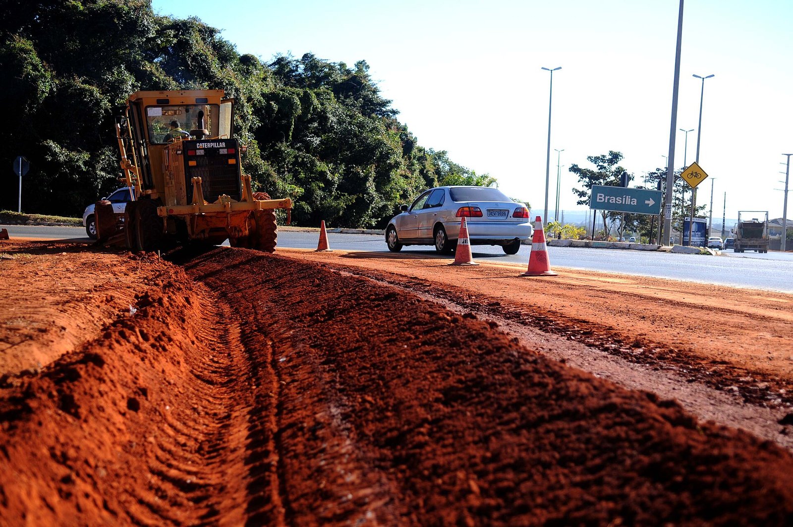 Obra em via de terra vermelha na região do Jardim Botânico e São Sebastião, com máquina, cones e placa indicando Brasília