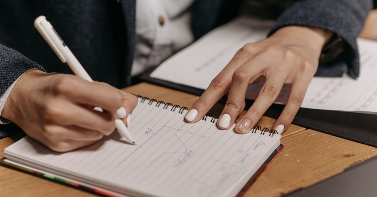 Mãos de mulher escrevendo em caderno sobre mesa de madeira