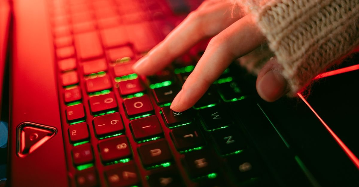 Mão digitando em teclado de notebook retroiluminado em ambiente escuro
