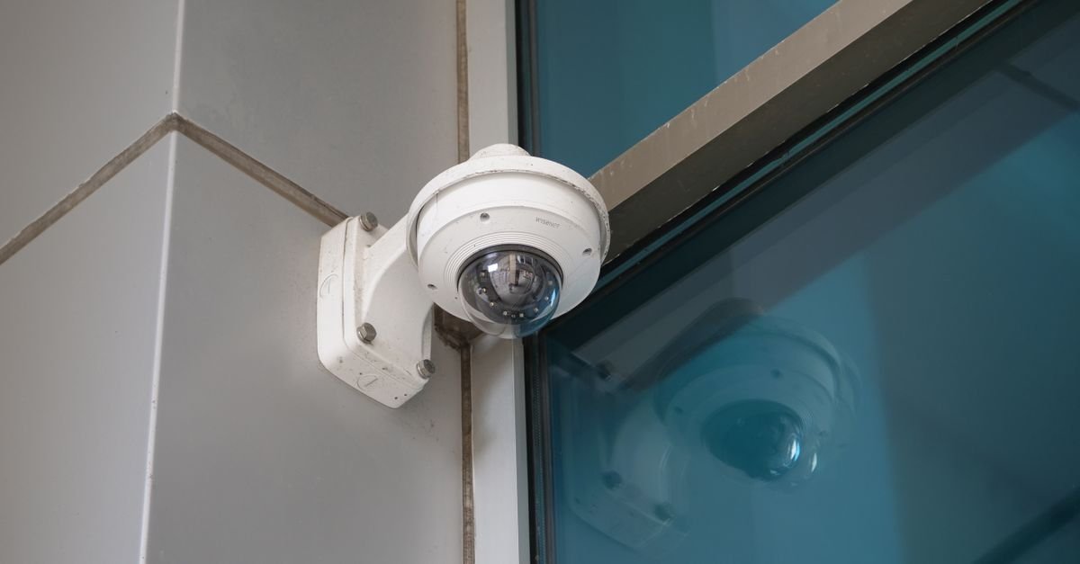 Camera de seguranca do tipo dome instalada na quina externa de um predio, ao lado de janela de vidro