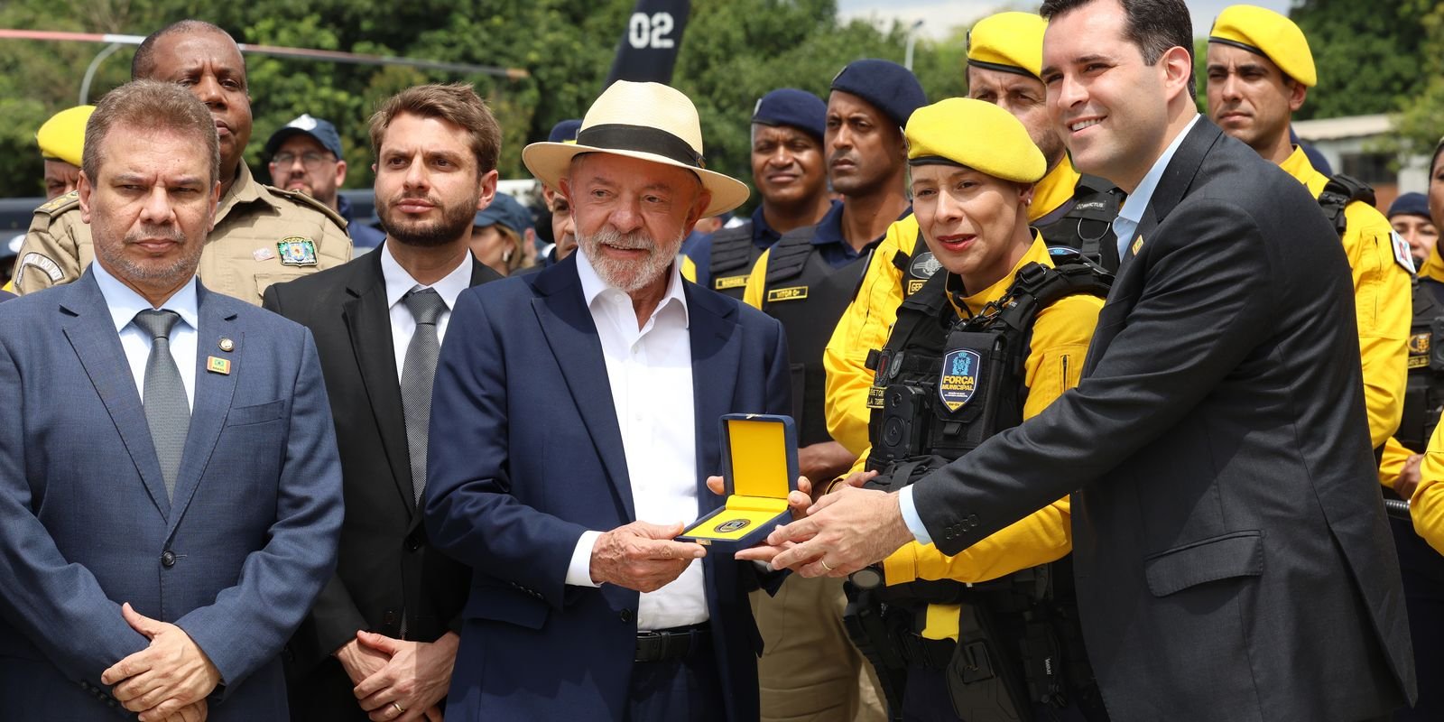 O presidente Lula recebe uma placa ao lado de agentes da Guarda Municipal fardados de amarelo, no Rio de Janeiro