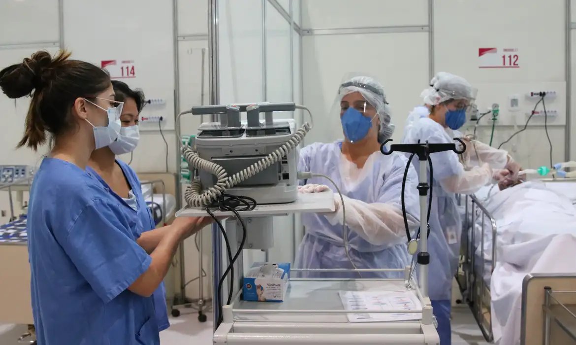 Equipe de saude com mascaras e aventais atende paciente em leito de UTI