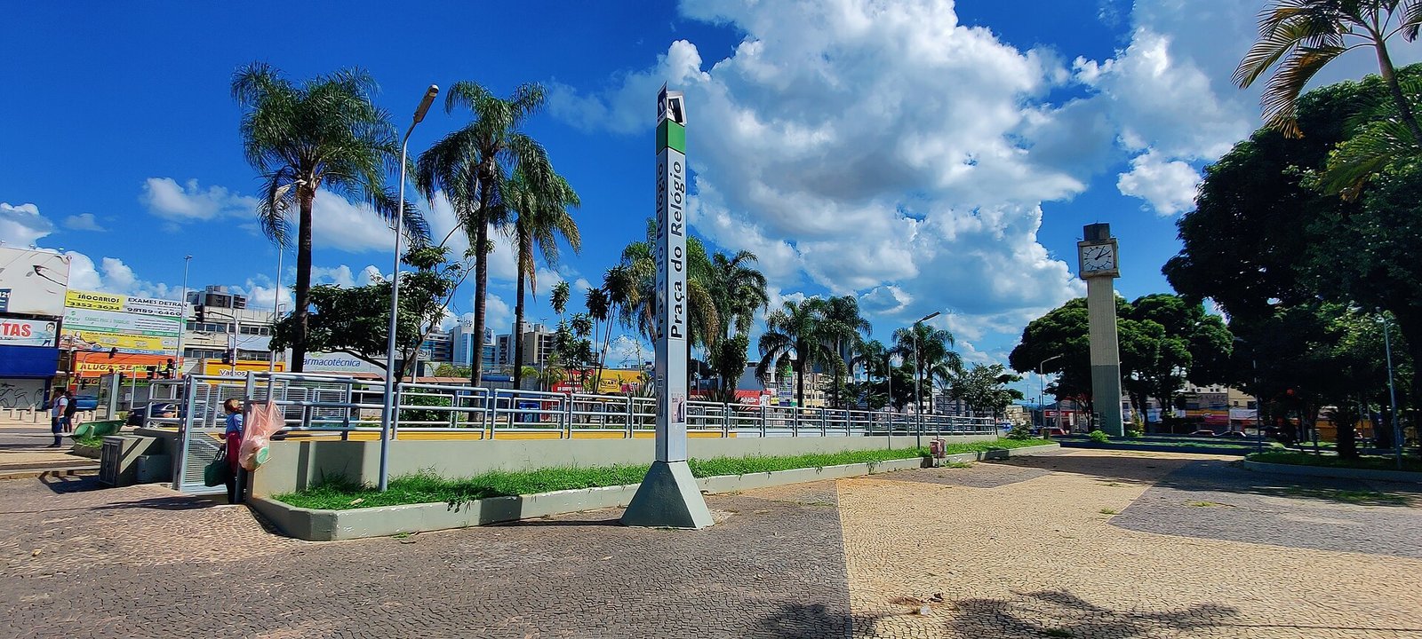 Totem da estação Praça do Relógio do metrô, em Taguatinga, com a torre do relógio ao fundo
