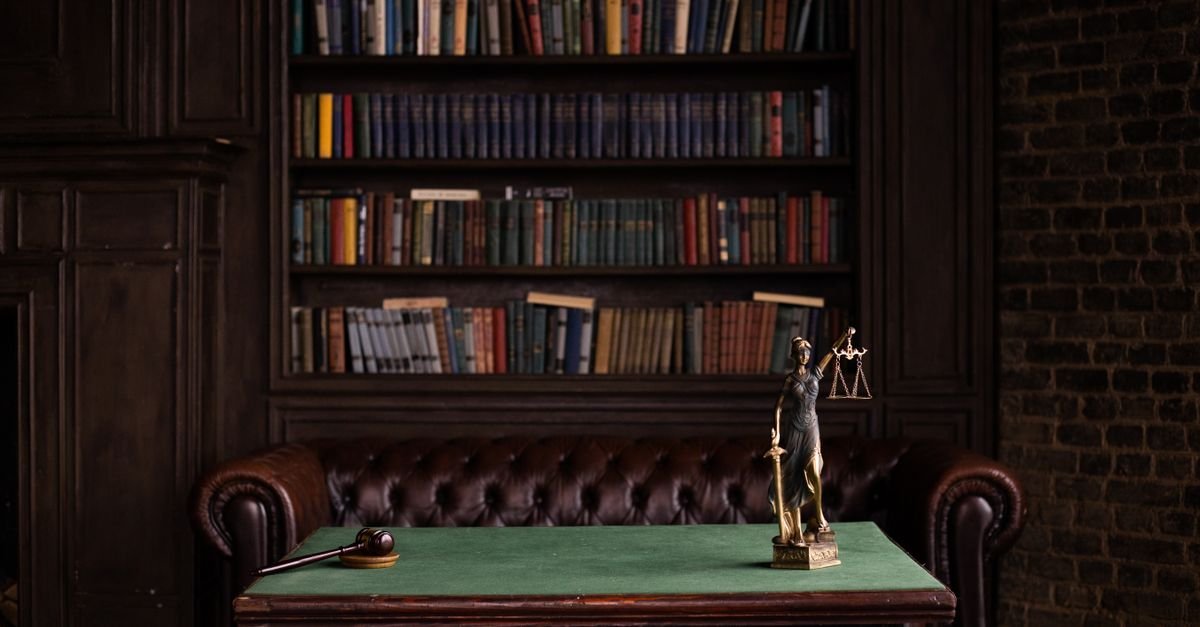 Estátua da Justiça e martelo de juiz sobre mesa em biblioteca de direito
