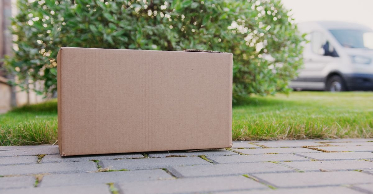 Caixa de papelão fechada sobre calçada, com veículo de entrega ao fundo