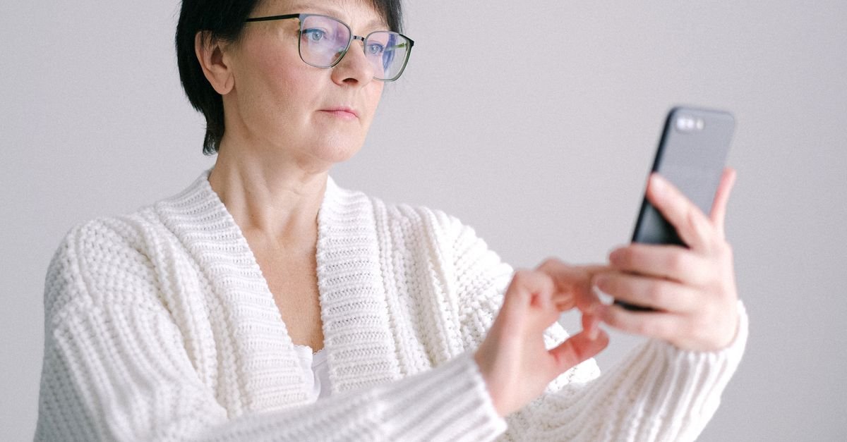 Aposentada de óculos consulta o celular, como no aplicativo Meu INSS