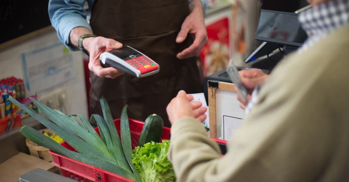 Atendente passa compras de cliente em caixa de supermercado com maquininha de cartão