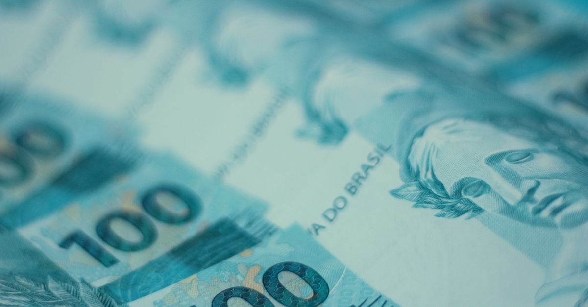 Cédulas de cem reais espalhadas em close, com destaque para o valor e a inscrição do Banco Central