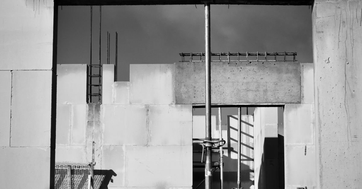 Imagem em preto e branco de obra de construção civil com paredes de concreto, escoras metálicas e andaimes