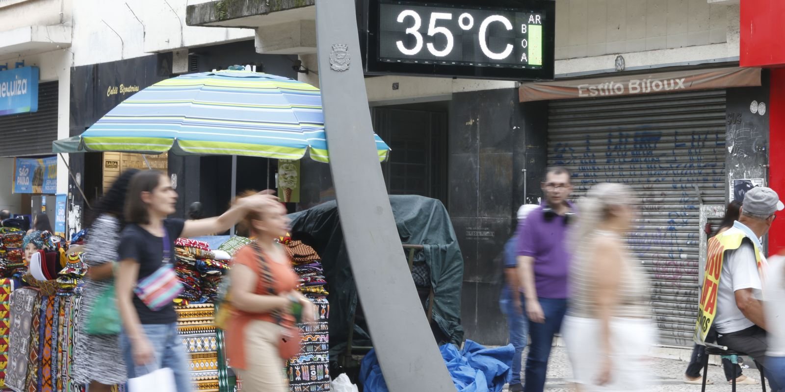 Termômetro de rua marca 35 graus em calçada movimentada do centro de São Paulo, com pedestres e barracas de comércio
