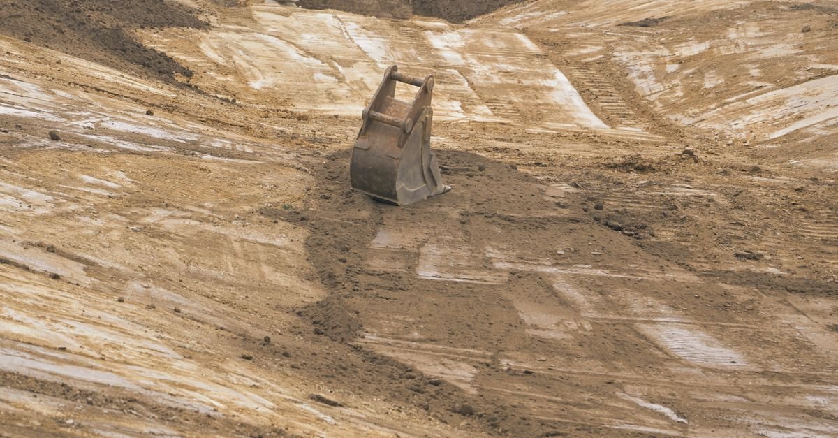 Caçamba de escavadeira apoiada sobre terreno de terra revirada