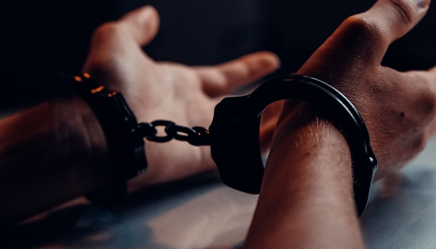Mãos algemadas apoiadas sobre uma mesa, em ambiente escuro