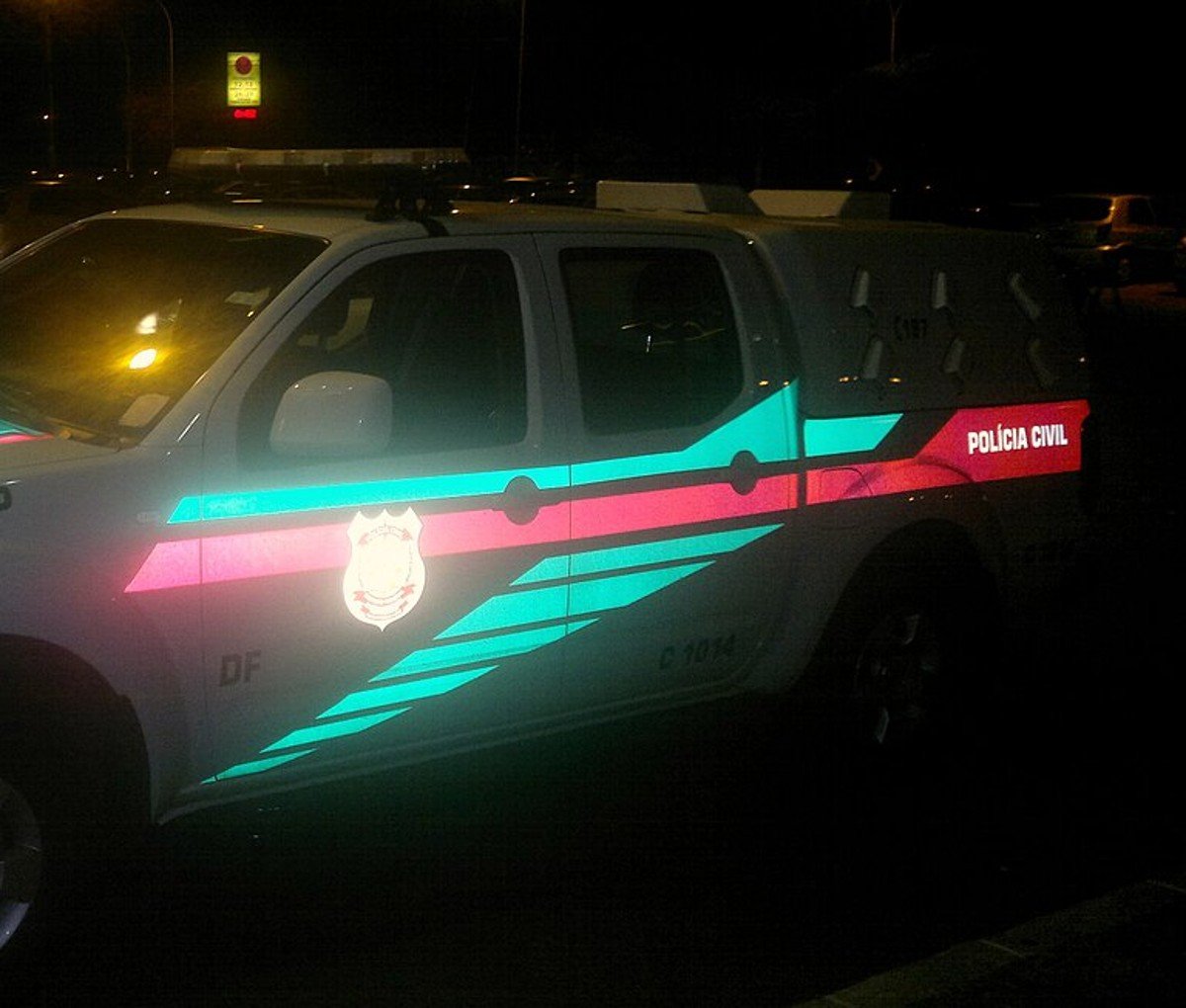 Viatura branca da Polícia Civil do Distrito Federal estacionada à noite, com faixa vermelha e brasão da corporação