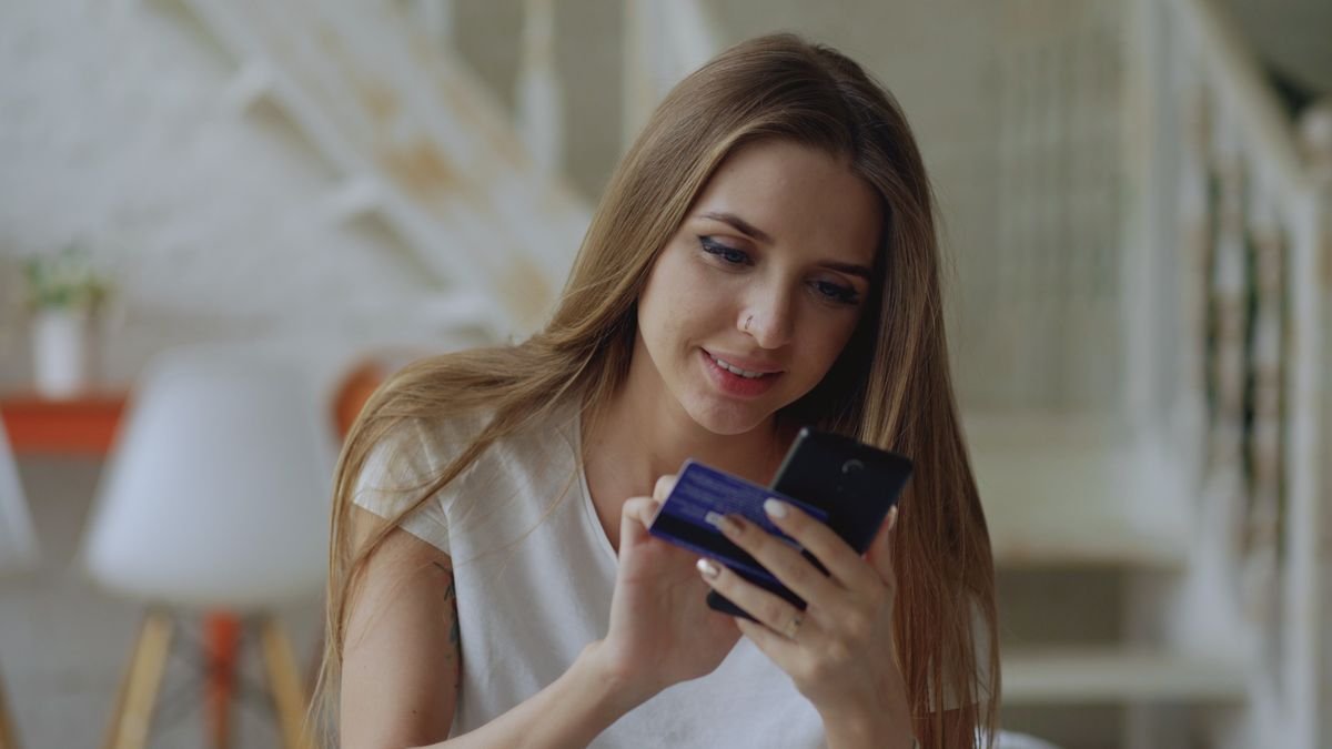 Mulher usando o celular com cartão na mão; imagem ilustrativa sobre o Caixa Tem