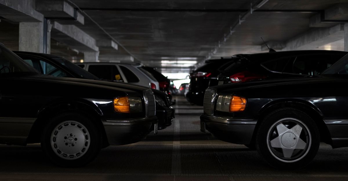 Carros clássicos escuros estacionados lado a lado em garagem de prédio