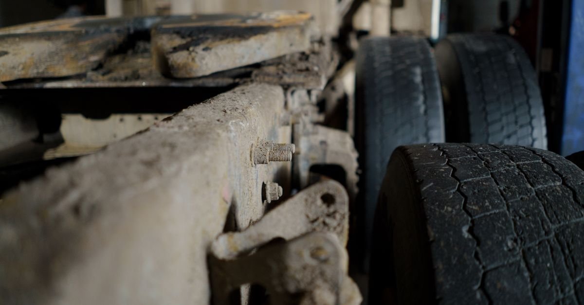Close do chassi e dos pneus traseiros de um caminhão de carga, com estrutura metálica em primeiro plano
