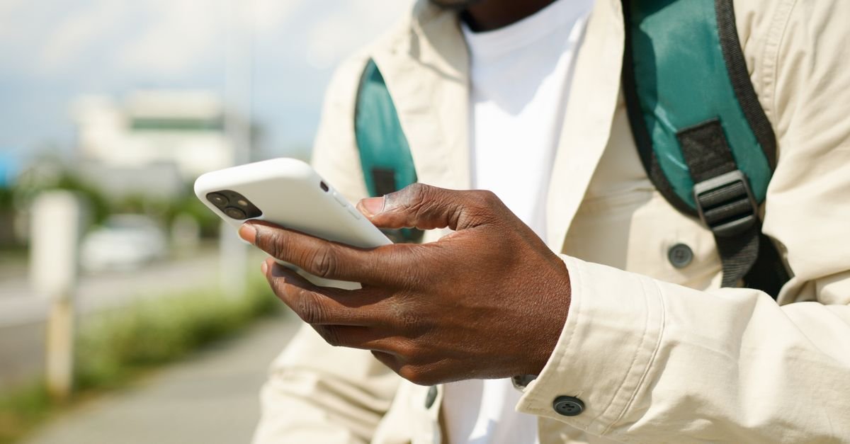 Mãos de uma pessoa usando um celular na rua durante o dia