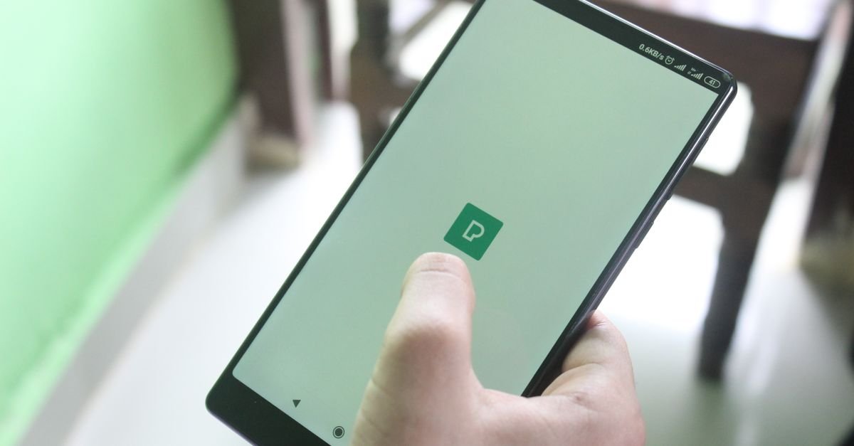 Mão segurando um celular com aplicativo aberto na tela, em ambiente interno