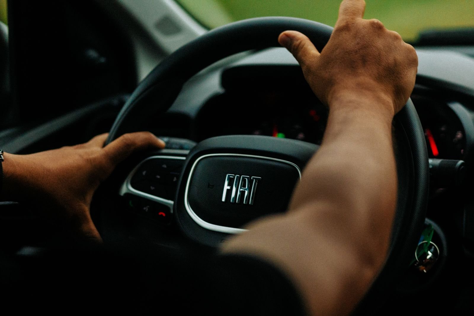 Mãos de um motorista no volante de um carro Fiat, com o painel desfocado ao fundo