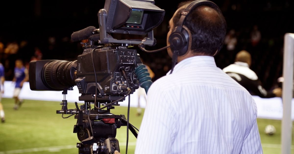 Cinegrafista opera câmera de transmissão à beira do gramado durante partida de futebol