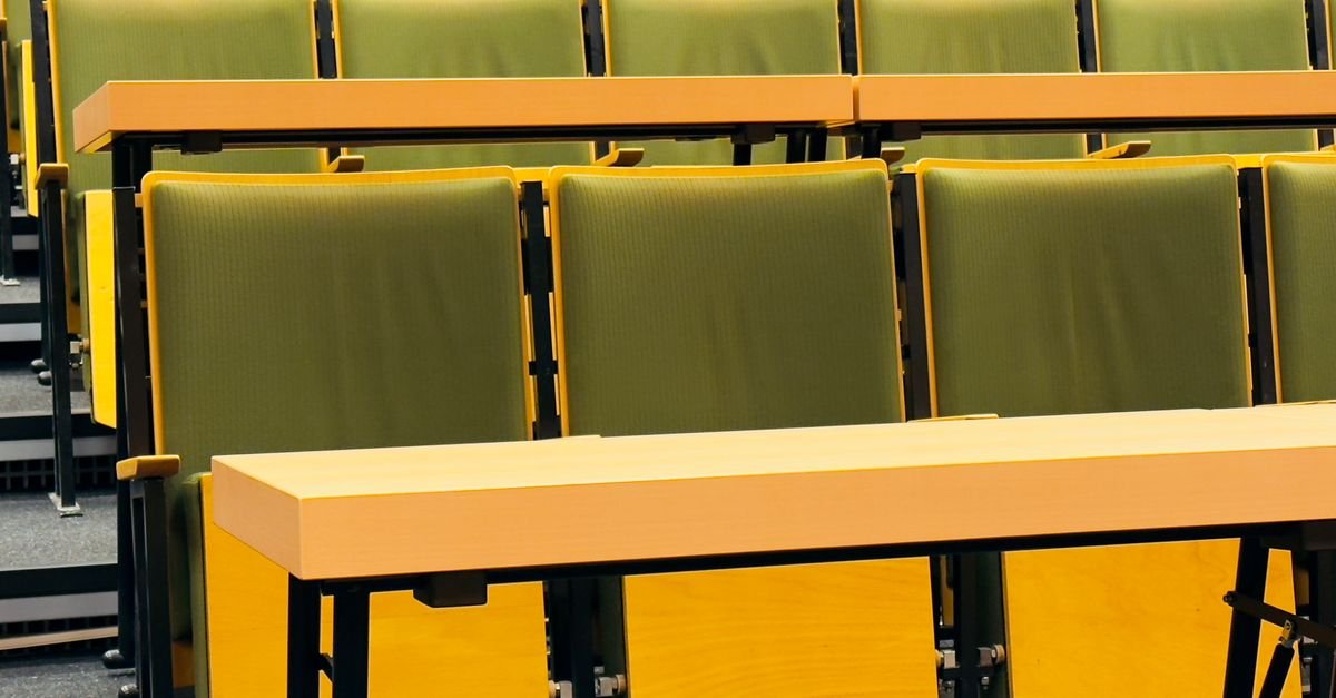 Fileiras de cadeiras verdes e bancadas de madeira vazias em auditório de faculdade