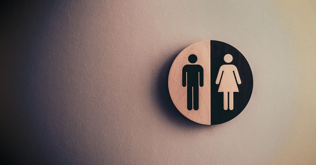 Placa circular de madeira em parede com os pictogramas masculino e feminino de banheiro