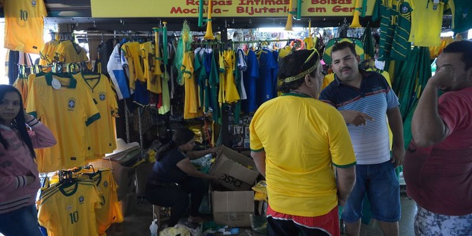 Loja com araras de camisas verde e amarelas da seleção brasileira e clientes no balcão