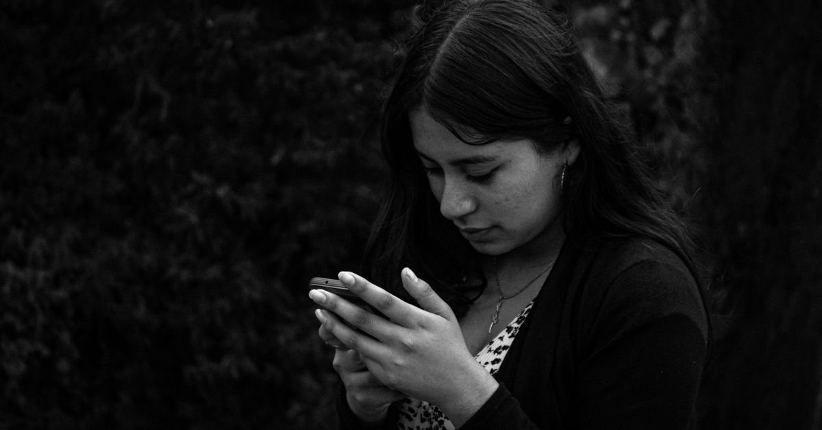 Jovem olha a tela do celular em imagem em preto e branco