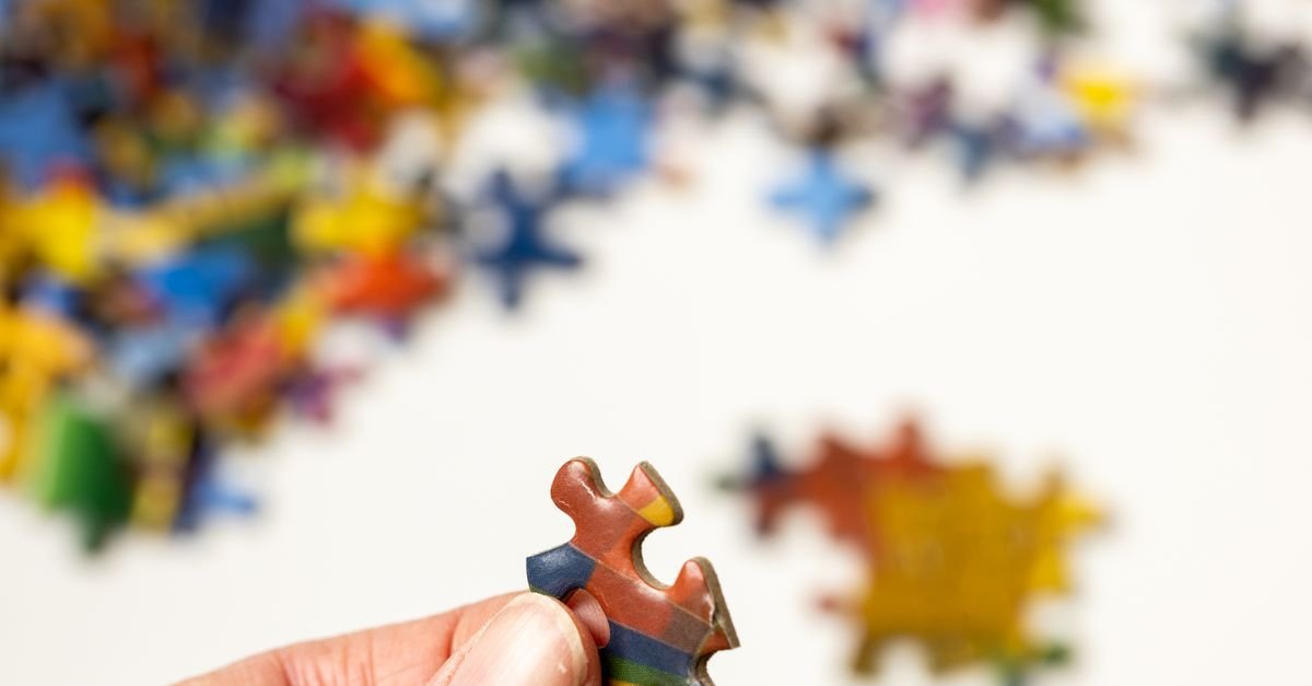 Mão segurando uma peça colorida de quebra-cabeça, com outras peças desfocadas ao fundo
