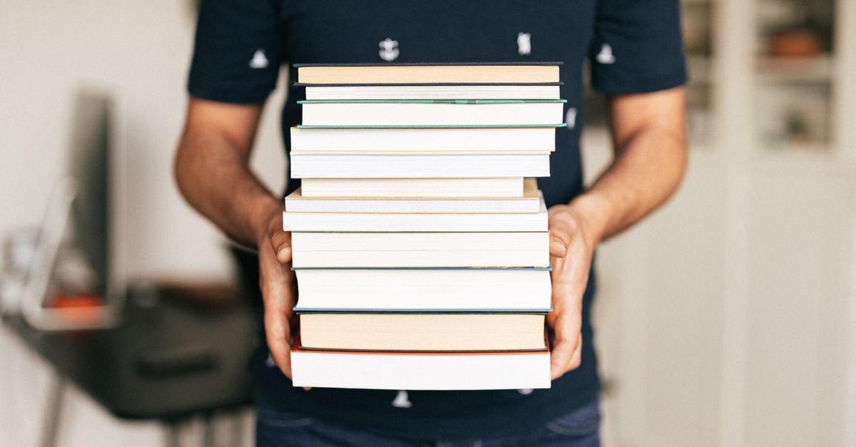Pessoa segurando uma pilha de livros didáticos